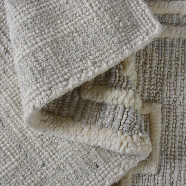 Chattan handwoven New Zealand wool rug with raised ivory diamonds on stone grey, in a living room