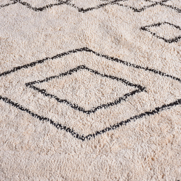 Chhapa tufted cotton rug with black diamonds and chevron borders on bone white, in a study