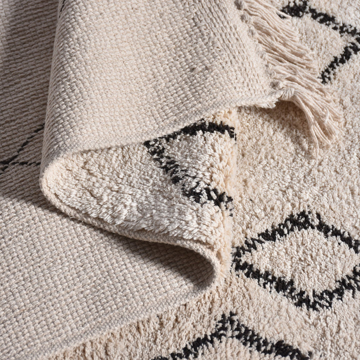 Chhapa tufted cotton rug with black diamonds and chevron borders on bone white, in a study