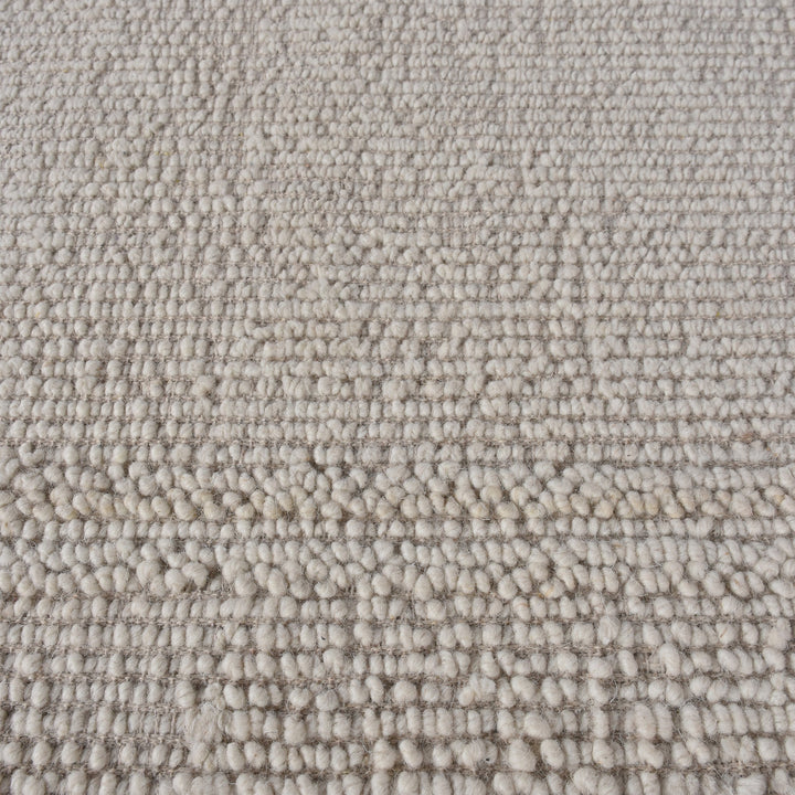 Linen handwoven wool rug in plain cream with a tonal border, in a bedroom