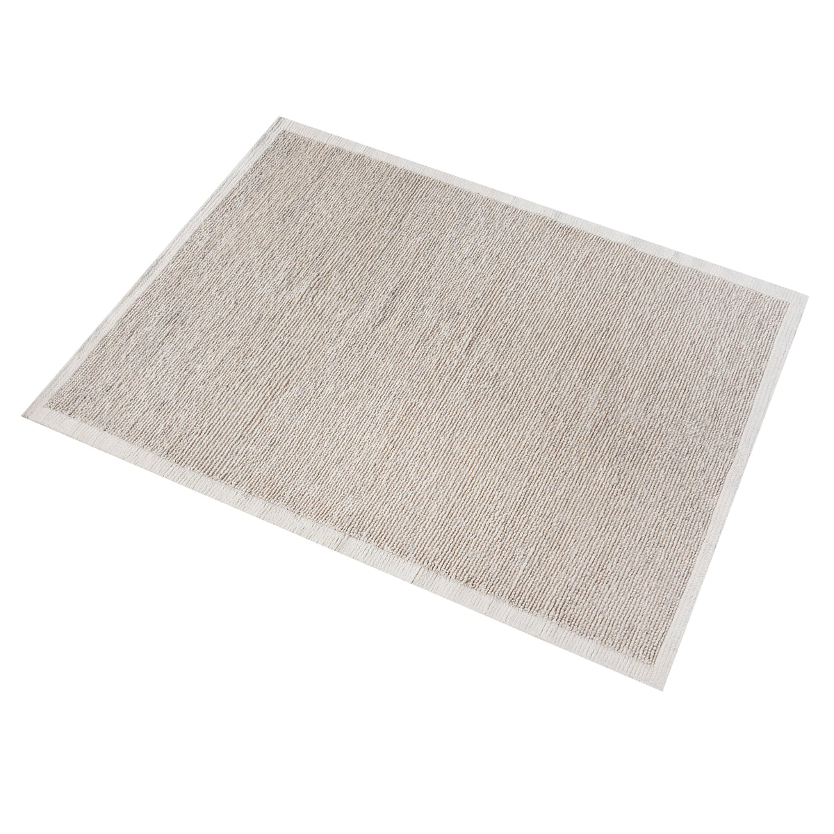 Shant handwoven flatweave wool rug in natural ivory with fine ribs and fringe, beside a bed