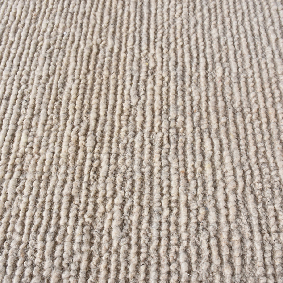 Shant handwoven flatweave wool rug in natural ivory with fine ribs and fringe, beside a bed