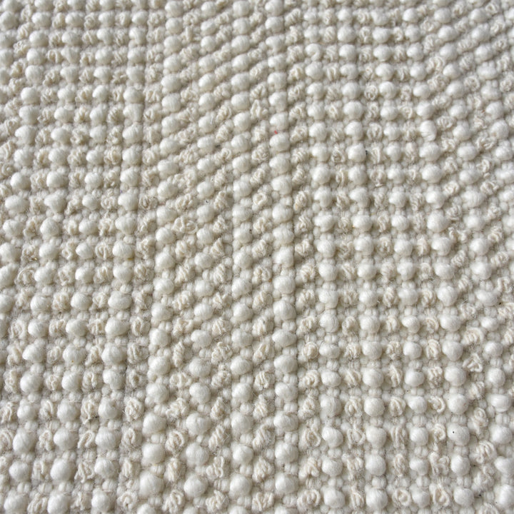 Basket handwoven cream wool rug with basketweave texture and tonal border, in a bedroom