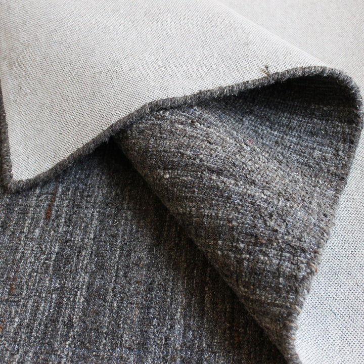 Saada handwoven flat wool rug in solid stone beige with charcoal, in a living room