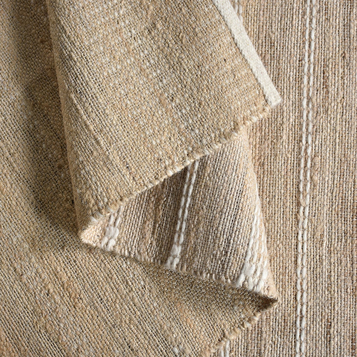 Taar handwoven wool and jute rug with fine vertical ribs in bleached natural and ivory, in a bedroom