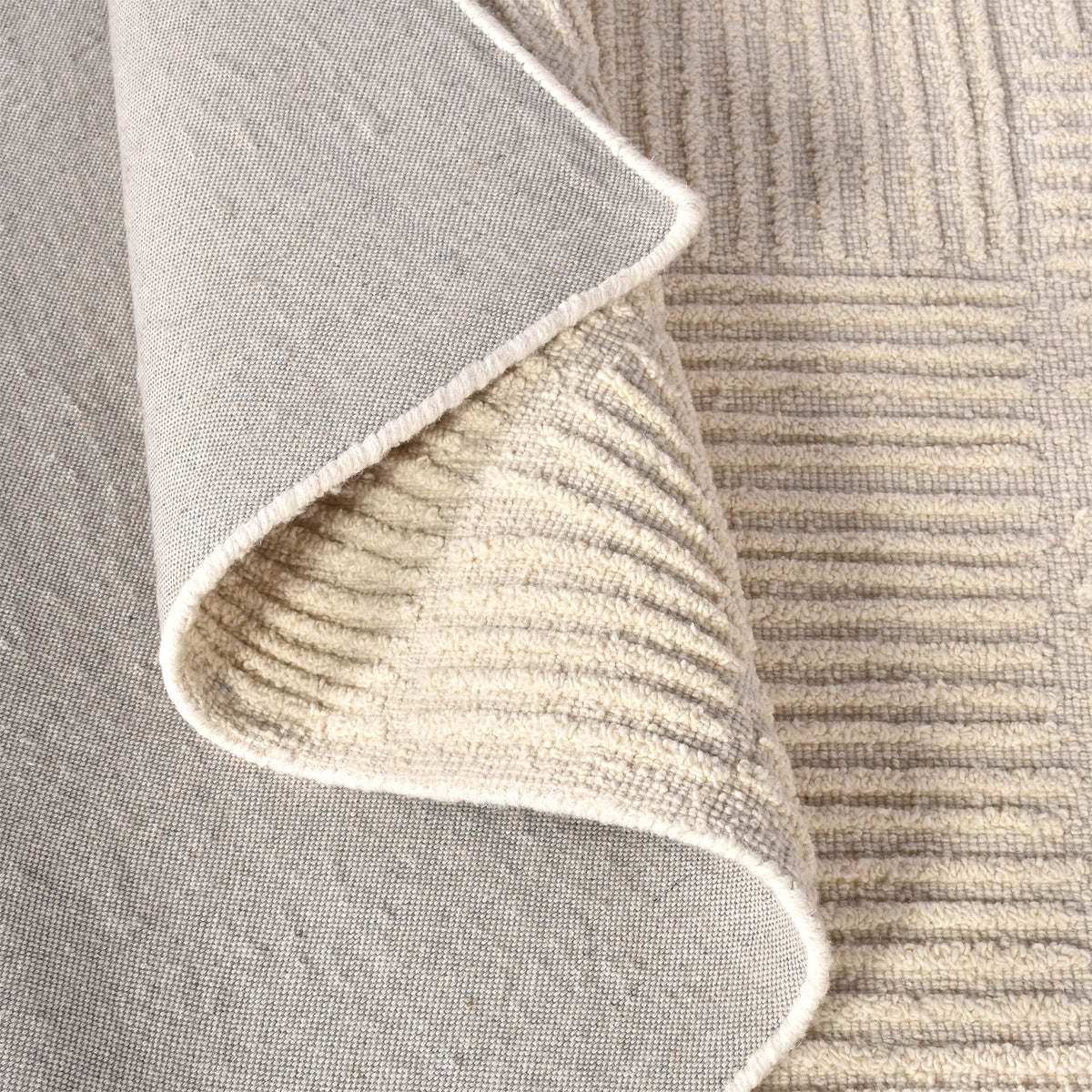 Kona handwoven cream wool rug with fine carved linear geometry, in a bedroom
