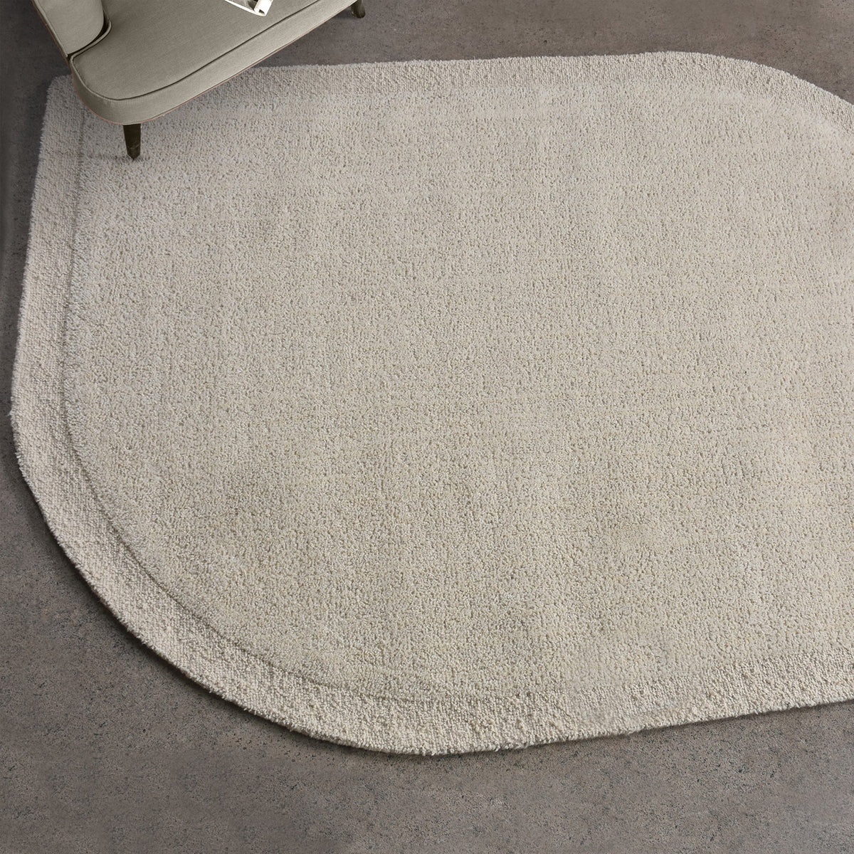Gol handwoven wool rug in plain cream with a soft cut pile and a curved edge, in a nursery