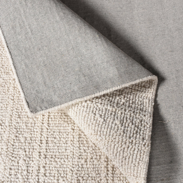 Oon handwoven ribbed wool rug in undyed oatmeal with horizontal ribs, under a coffee table