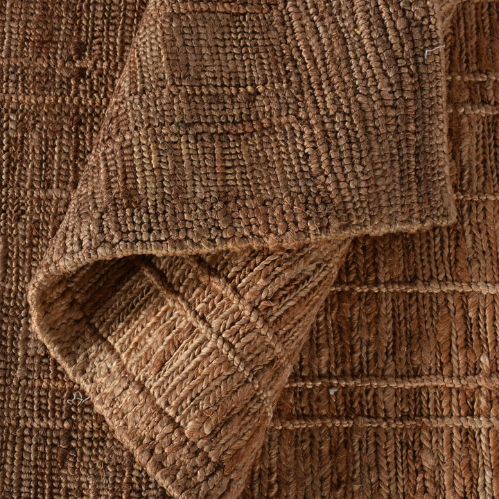 Geru hand-knotted jute rug in burnt sienna and tan with a rustic high pile, in a living room