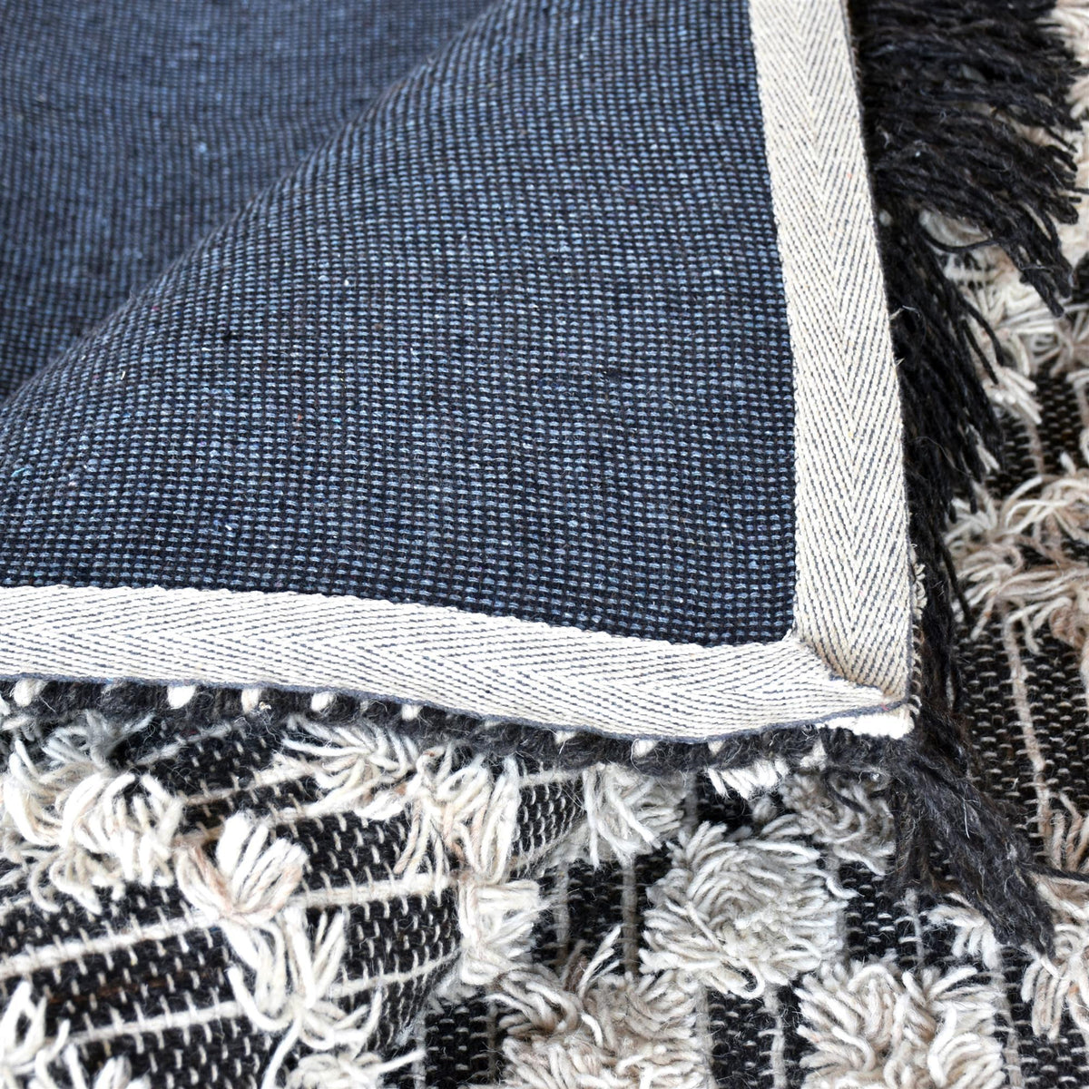 Tassel tufted wool rug with charcoal and ivory chevrons and shaggy bands, in a bedroom