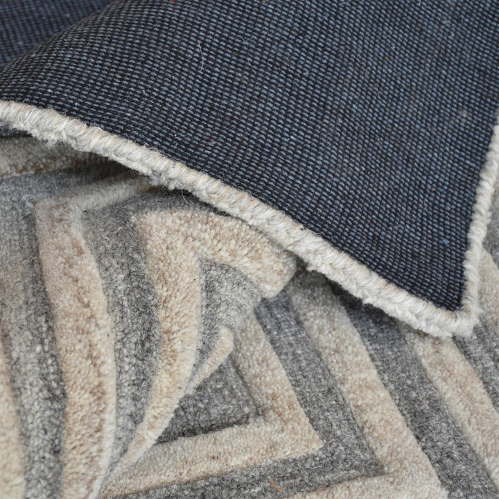 Raasta hand-tufted sand beige wool rug with carved concentric maze lines, in a living room