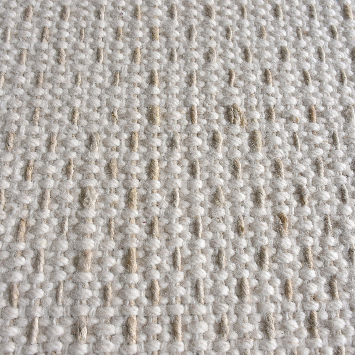 Kankar handwoven wool and jute rug in pale ivory-grey with a pebbled loop weave, in a bedroom