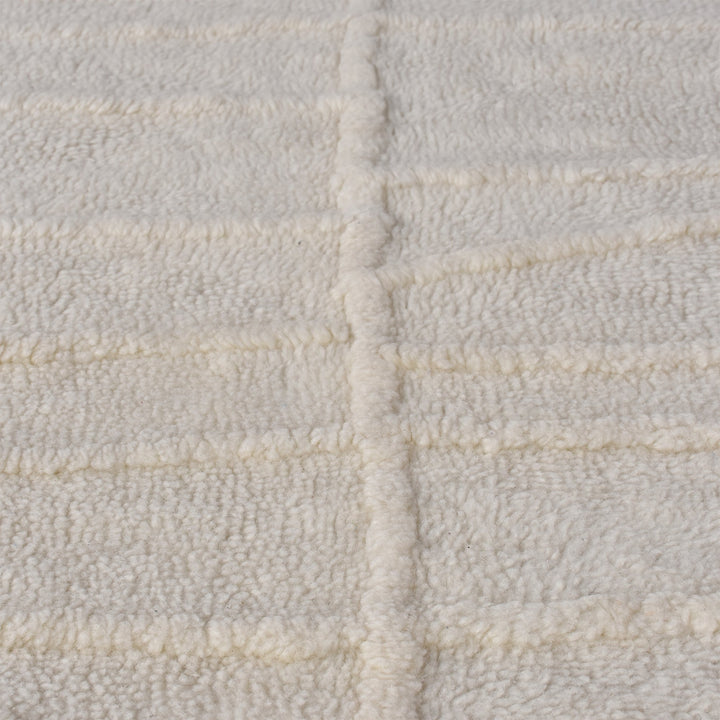 Swell tufted ivory New Zealand wool rug with carved waves and fringe, in a living room