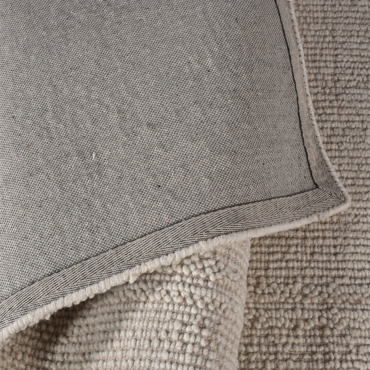 Linen handwoven wool rug in plain cream with a tonal border, in a bedroom