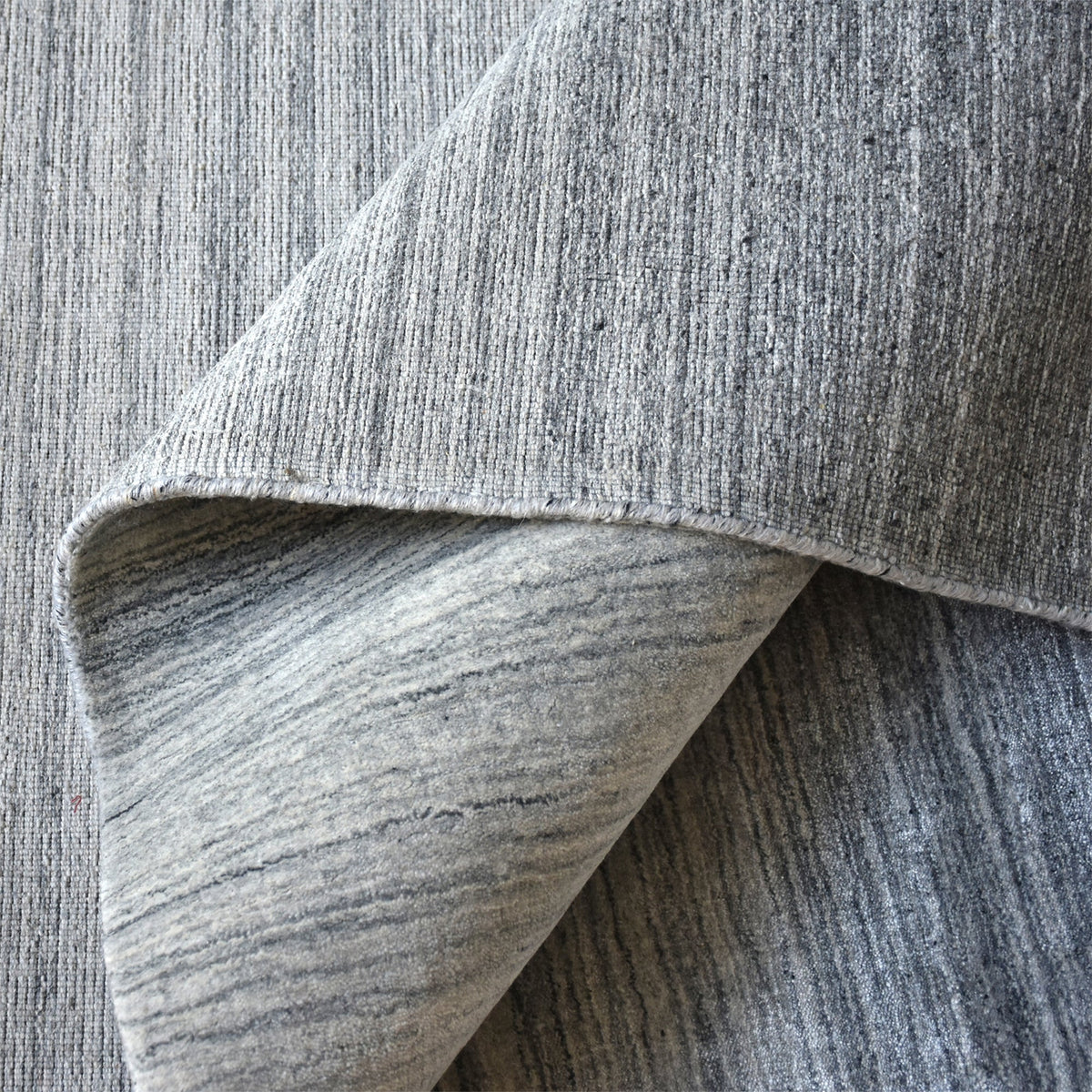 Baadal handwoven wool and viscose rug in streaked grey, charcoal and silver, in a living room