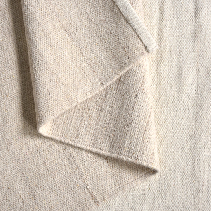 Kamaan handwoven wool flatweave rug with overlapping ivory and beige arcs, in a living room